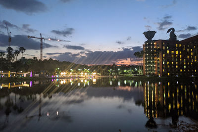 Illuminated buildings by lake against sky at dusk