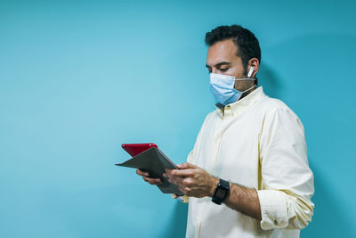 Portrait of a young businessman with a mask using a tablet and h