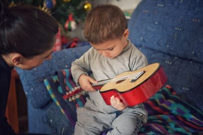 Cute boy playing guitar with mother at home