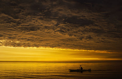 Silhouette man sailing in boat on sea against cloudy sky during sunset