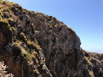 Low angle view of rocky mountains against clear blue sky