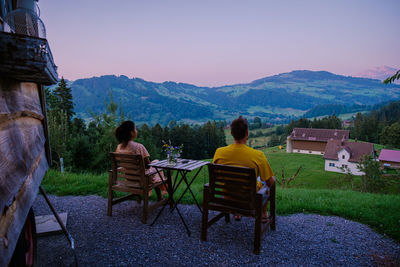 Rear view of people sitting on table against mountains