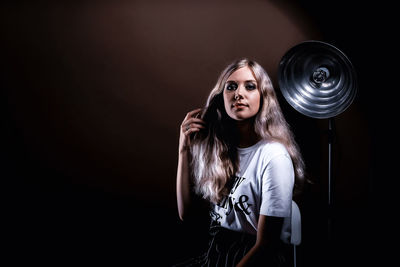 Portrait of young woman standing against black background