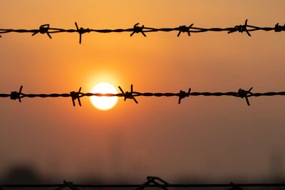 Silhouette barbed wire against sky during sunset
