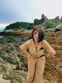 Portrait of young woman standing on rock against sky