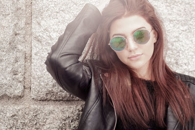 Close-up portrait of young woman in sunglasses against wall