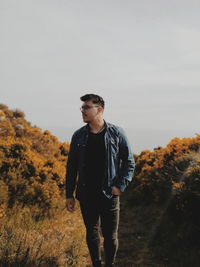 Young man looking away while standing on land against sky