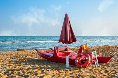 Parasol and red boats on beach against sky