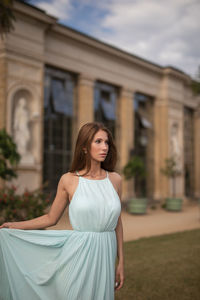 Portrait of young woman standing against building