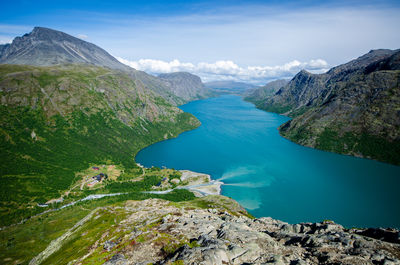 Scenic view of a mountain hut beside a long turquoise lake between mountains.