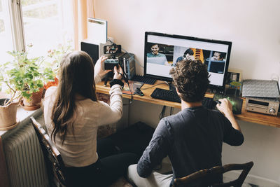 High angle view of friends blogging over camera while looking on smart phone in house