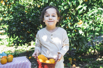 A little boy is holding a basket of bright oranges in his hands.