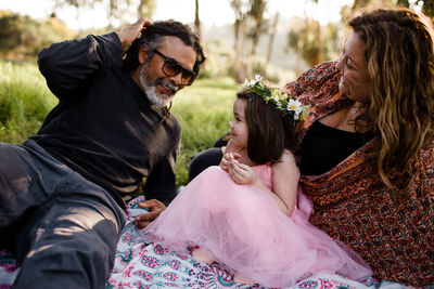 Aunt, uncle and niece sitting on blanket in field