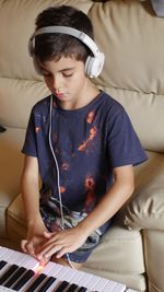 Boy with headphones practicing piano on sofa at home
