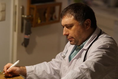 Side view of mature doctor with pen sitting in hospital