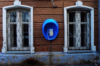 Blue pay phone on wall amidst windows