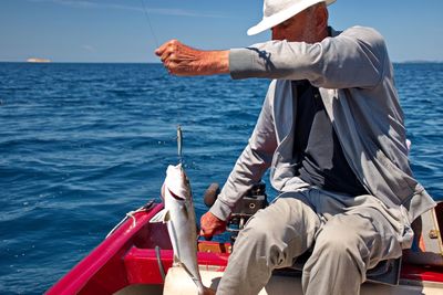 Old fisherman sitting in a boat and holding fish on hook