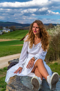 Thoughtful beautiful woman sitting on rock against sky