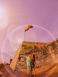 Low angle view of couple kissing with columbian flag in background against sky