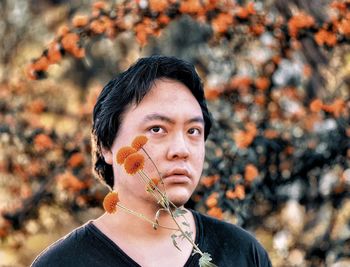 Portrait of young asian man with orange flowers against orange rowan berry trees.