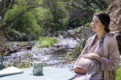 Pregnant woman with hands on stomach sitting in forest