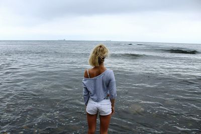 Rear view of young woman standing at beach against sky