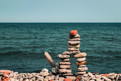 Stack of pebbles on rock by sea against clear sky