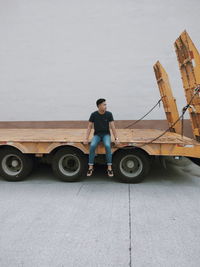 Young man looking away while sitting on truck against sky