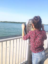 Rear view of man sitting on railing by sea