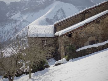 House on snow covered field by houses against mountain