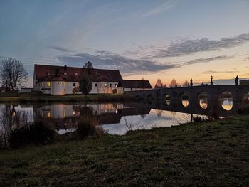 Buildings by river against sky during sunset