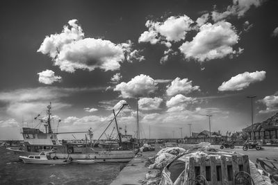 Boats in harbor against cloudy sky