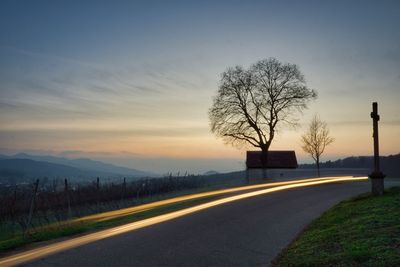 Road by silhouette trees against sky at sunset