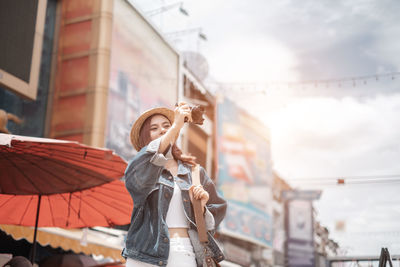 Woman with umbrella standing against sky in city