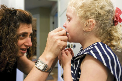 Close-up of mother removing daughter's teeth at home