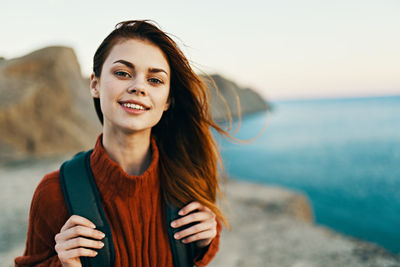 Portrait of smiling young woman standing against sea