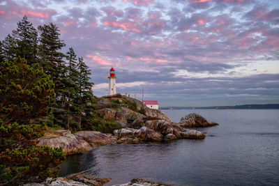 Lighthouse by sea against sky during sunset