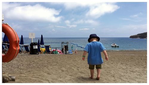 Rear view of boy in hat walking at beach against sky