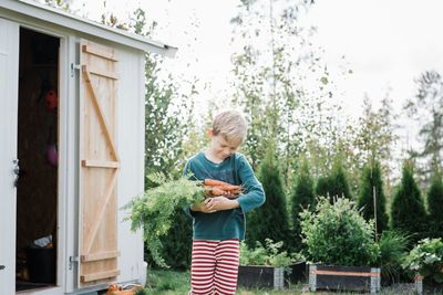 Full length of boy standing by plants against trees