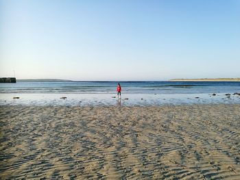 Girl walking on shore at beach against sky