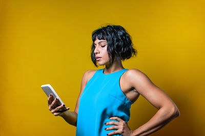 Young woman using mobile phone against yellow background