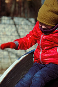 Cute boy wearing warm clothing while sitting on slide in playground