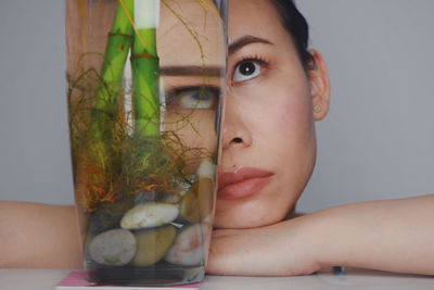 Close-up of woman face by glass container on table