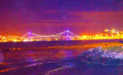 Illuminated bridge over river against sky