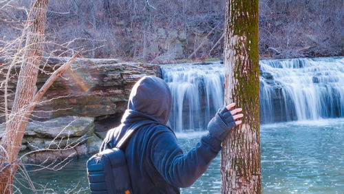 Rear view of man standing by waterfall in forest