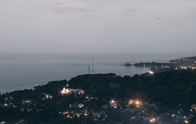 Illuminated city by sea against sky at night