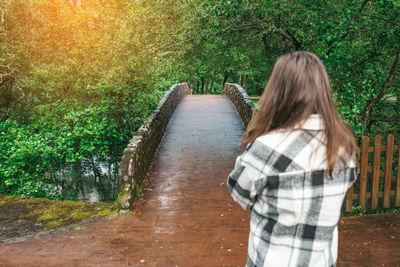 Young woman on a plaid shirt walking by a stone bridge in the forest