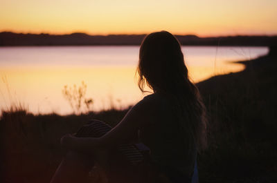 Woman sitting against lake during sunset