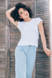 Portrait of young woman with curly hair standing against wooden door