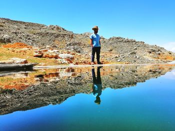 Man standing by lake against clear blue sky